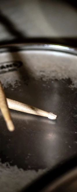 A pair of wooden drumsticks resting on a worn snare drum surface, showing signs of frequent use. A pair of wooden drumsticks resting on a worn snare drum surface, showing signs of frequent use.